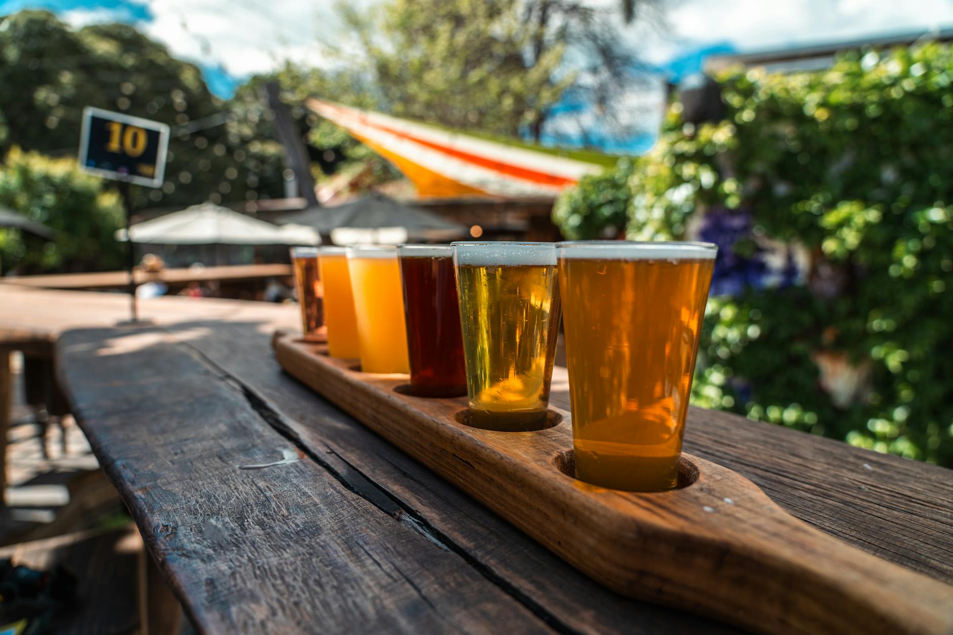 A flight of beers on a wooden table at an outdoor bar